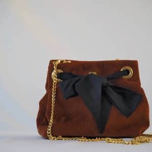 Sac seau en velours orange brûlé / rouille porté croisé par une chaine dorée. Fermeture par un bandeau en tissu plumetis bleu nuit.