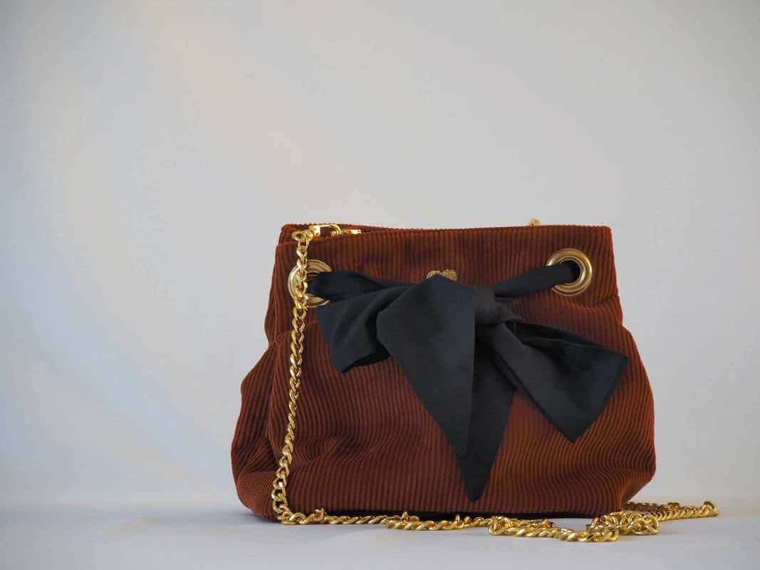 Sac seau en velours orange brûlé / rouille porté croisé par une chaine dorée. Fermeture par un bandeau en tissu plumetis bleu nuit.