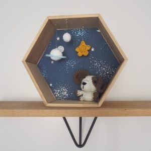 Décoration enfant. Petit chien réalisé au crochet dans cadre hexagonal. Le fond du cadre est tapissé d'un papier peint représentant des étoiles et des planètes. Le personnage au crochet est fixé au cadre. Suspendu au cadre 2 planètes et une étoile réalisés au crochet.
