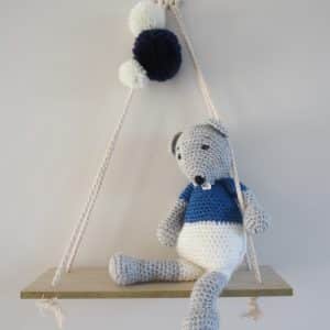 Souris grise, blanc et bleue au crochet fixée sur une balancelle en bois. Pompons blancs et bleu marine fixés au cordage.