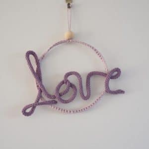Décoration murale. Mot love en tricotin, de couleur violette. Le mot love est fixé à un cercle métallique.