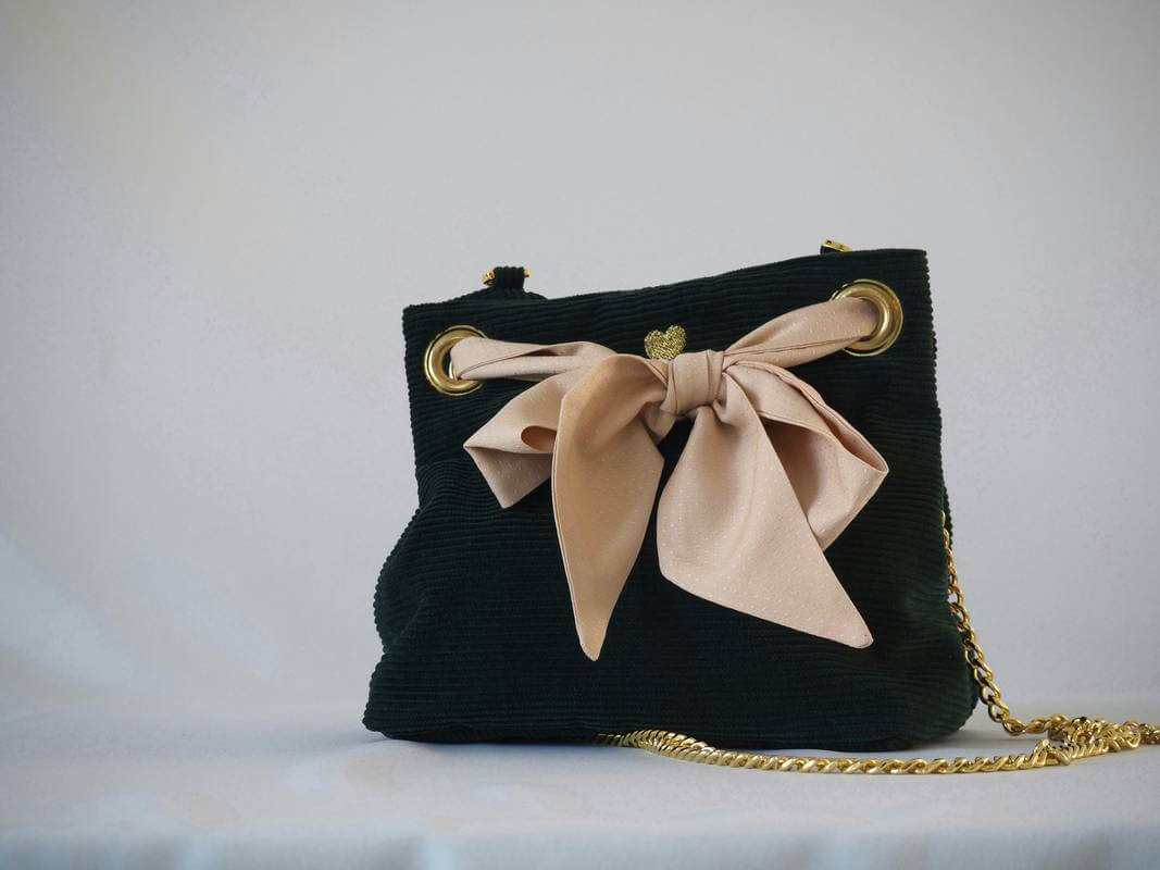 Sac seau en velours vert sapin porté croisé par une chaine dorée. Fermeture par un bandeau en tissu plumetis blush/nude