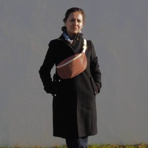 Sac banane fanny brun rosé porté sur un manteau noir