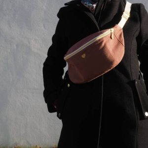 Sac banane fanny brun rosé porté sur un manteau noir