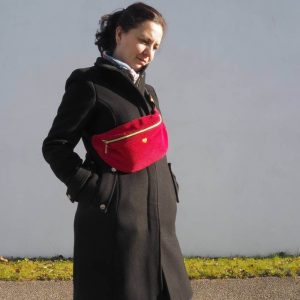 Sac banane Fanny, en velours côtelé rouge, porté une sur un manteau noir, permettant de réhausser une tenue