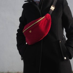 Sac banane Fanny, en velours côtelé rouge, porté une sur un manteau noir, permettant de réhausser une tenue