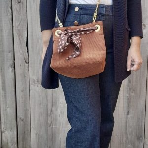 Sac seau en velours orange brûlé / rouille porté croisé par une chaine dorée. Fermeture par un bandeau en tissu marron, petites fleurs blanches.
