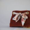Sac seau en velours orange brûlé / rouille porté croisé par une chaine dorée. Fermeture par un bandeau en tissu multicolore rosé orangé.