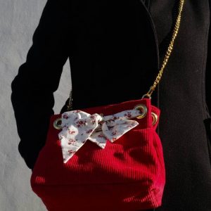 Sac seau en velours rouge avec lien en tissu et chaine dorée porté sur un manteau noir