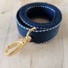 Bandoulières, anses réglables. Coloris : Bleu marine, liserés blancs Bouclerie dorée.