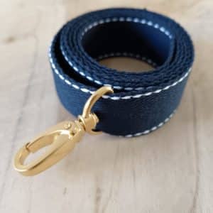 Bandoulières, anses réglables. Coloris : Bleu marine, liserés blancs Bouclerie dorée.