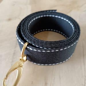Bandoulières, anses réglables. Coloris : noir, liserés blancs Bouclerie dorée.