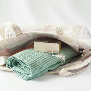 Sac cabas en polyester et coton recyclés, de couleurs pastels (rose, jaune, violet, vert d'eau), avec fermeture par zip contenant des affaires de plage