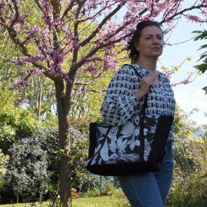 Sac cabas noir à motif tropical porté sur une chemise blanche et bleue et un jean bleu.