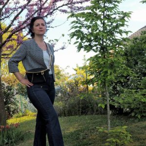 Sac banane noir, élégant, avec passepoil doré porté avec un jean, un haut blanc et une veste coute en jacquard noir et blanc.