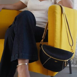 Sac banane noir avec passepoil doré posé sur le bord d'un fauteuil moutarde.