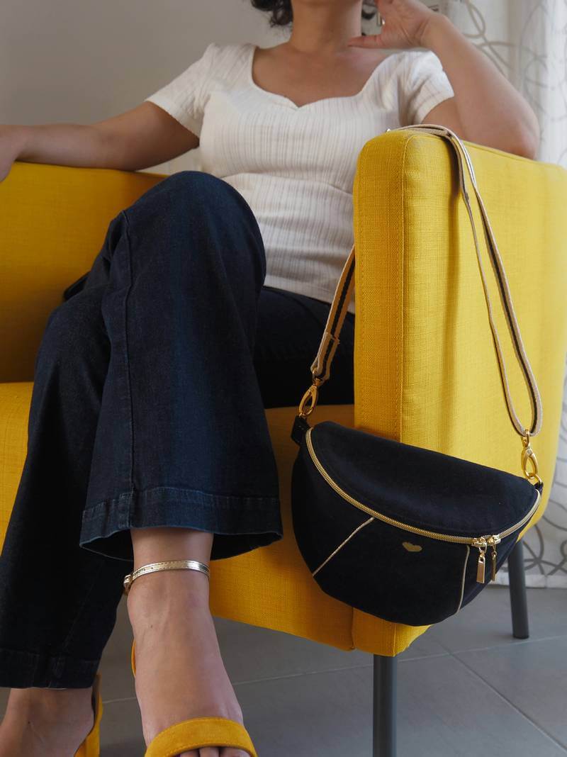 Sac banane noir avec passepoil doré posé sur le bord d'un fauteuil moutarde.