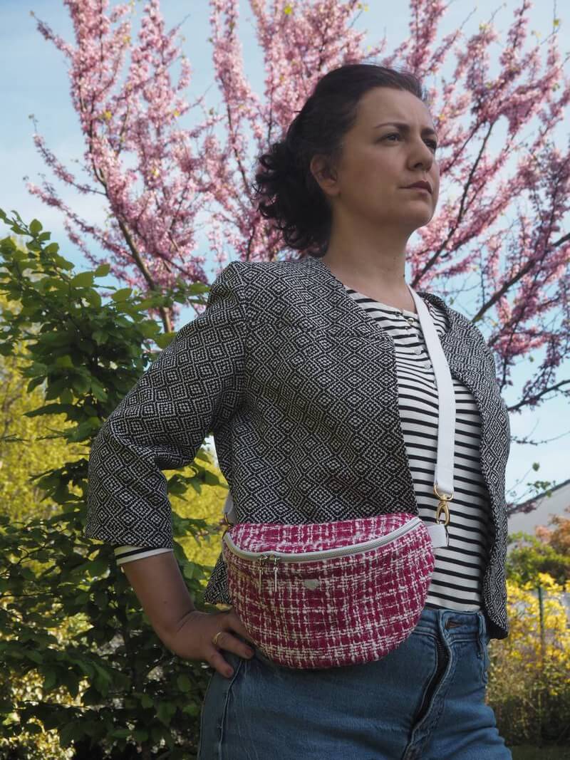 Banane élégante en tweed de couleur fuchsia portée sur une veste coute en jacquard noir et blanc et un pantalon jean.
