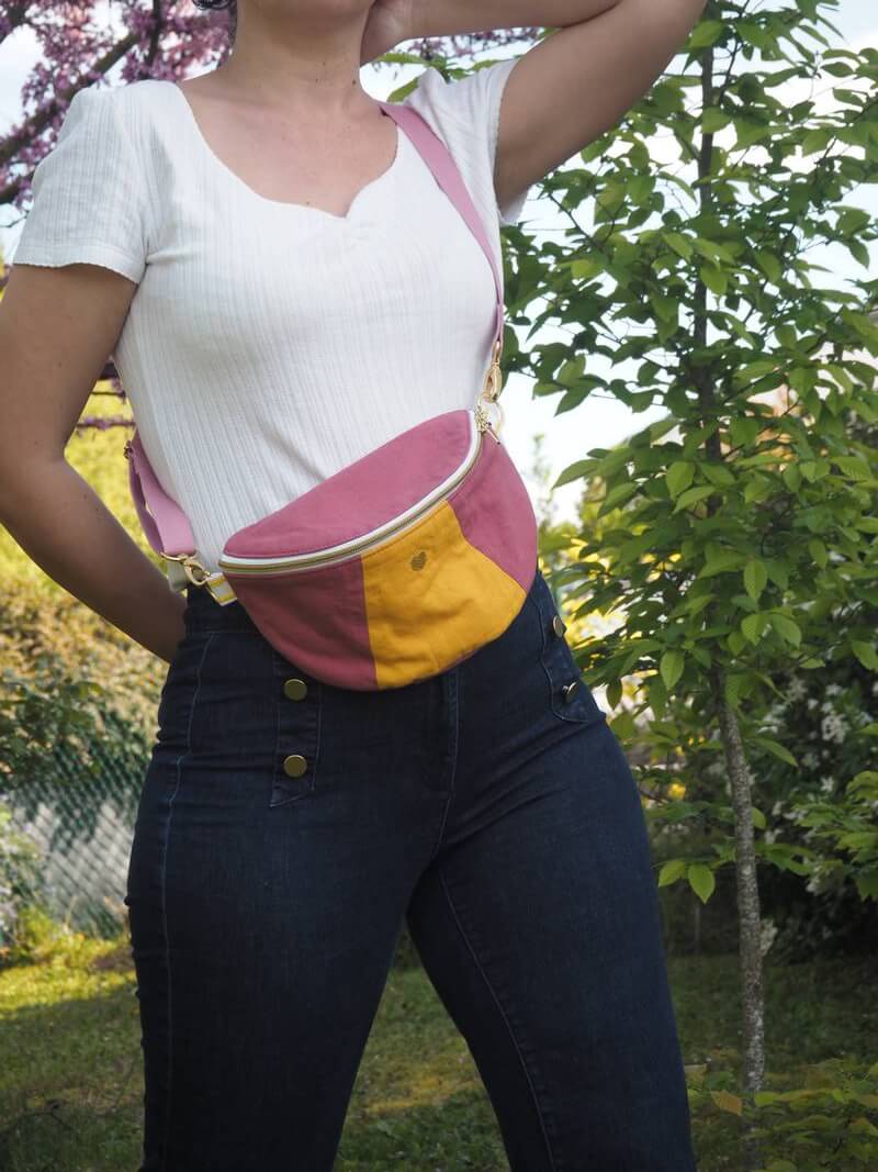Sac banane 90's rose et jaune avec bandoulière amovible portée en cross body sur un haut blanc et un jean brut.