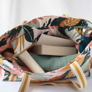 Sac cabas en coton enduit, de cmotif tropical multicolor (rose, vert, moutarde,...) , avec fermeture par zip. Présenté avec des affaires de plage.