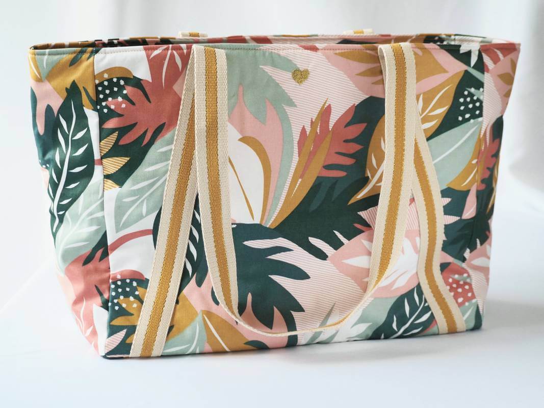 Sac cabas en coton enduit, de motif tropical multicolor (rose, vert, moutarde,...), avec fermeture par zip. Vue de devant avec la broderie coeur.