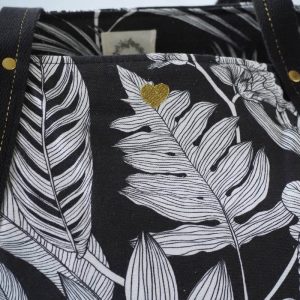 Sac cabas noir à motif tropical. Zoom sur les détails : broderie coeur dorée, anse en coton noir avec un liseré doré.