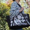 Sac cabas noir à motif tropical porté sur une chemise blanche et bleue et un jean bleu.