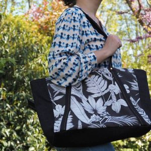 Sac cabas noir à motif tropical porté sur une chemise blanche et bleue et un jean bleu.