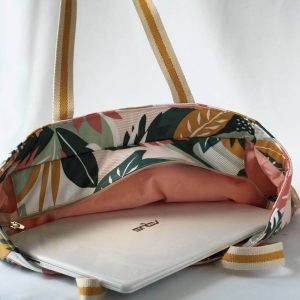 Sac cabas en coton enduit, de motif tropical multicolor (rose, vert, moutarde,...), avec fermeture par zip. Présenté avec des affaires de bureau.