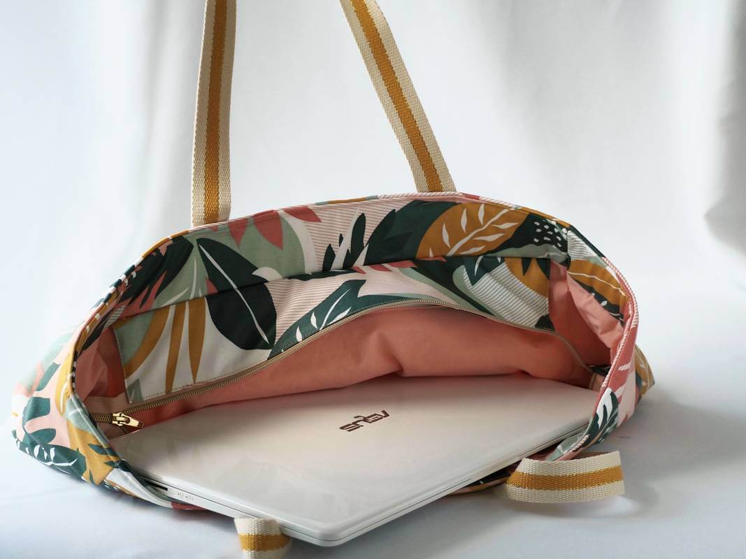 Sac cabas en coton enduit, de motif tropical multicolor (rose, vert, moutarde,...), avec fermeture par zip. Présenté avec des affaires de bureau.